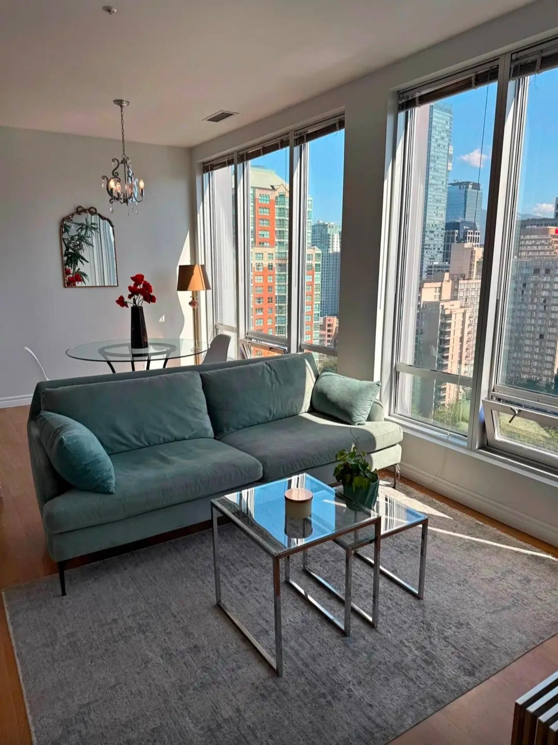 A modern living room with a green sofa, a glass coffee table, and a view of tall buildings.