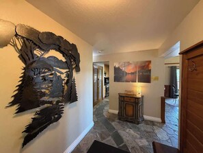 A hallway with a unique wall art, a stone floor, a wooden door, and a small table with a lamp. - Ember Creek 3 Bedroom & Loft, Family Retreat! (Shaver Lake)