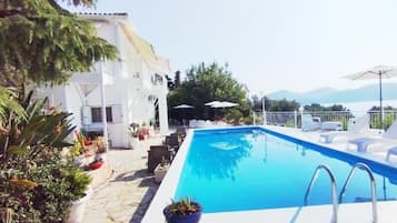 A swimming pool with lounge chairs, a white building, and a mountainous backdrop.