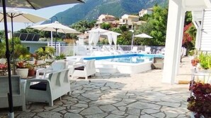 A pool area with lounge chairs, umbrellas, and a view of mountains. - Xenia & Antonis  (Nikiana)