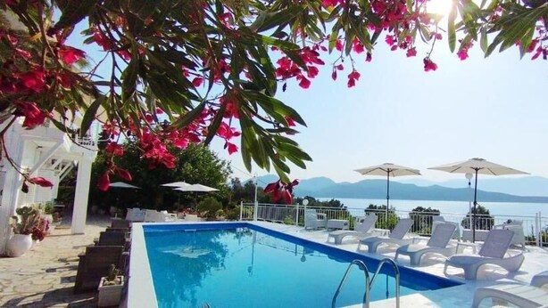 A pool with lounge chairs and umbrellas, a white building, and a view of the sea and mountains. - Xenia & Antonis  (Nikiana)
