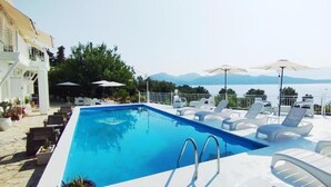 A rectangular swimming pool with a view of mountains, surrounded by white lounge chairs and umbrellas. - Xenia & Antonis  (Nikiana)