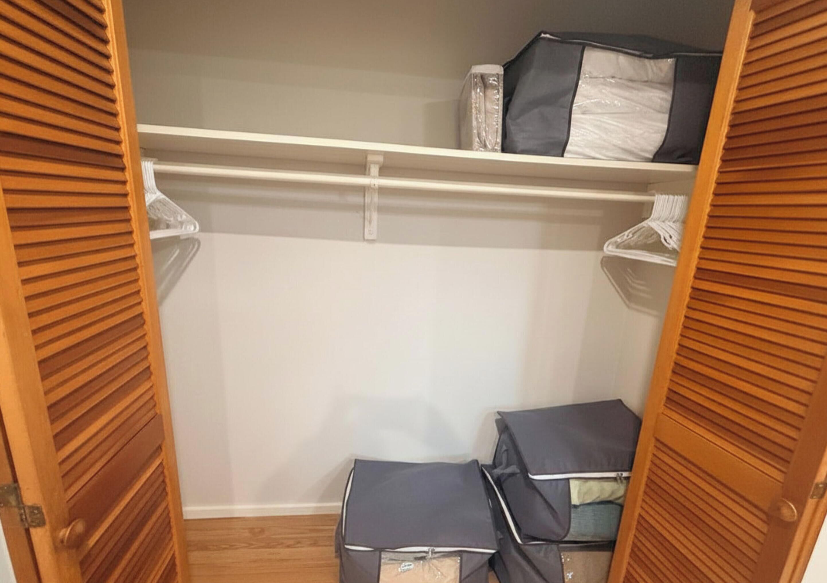 A closet with wooden doors, a white shelf, and storage boxes.