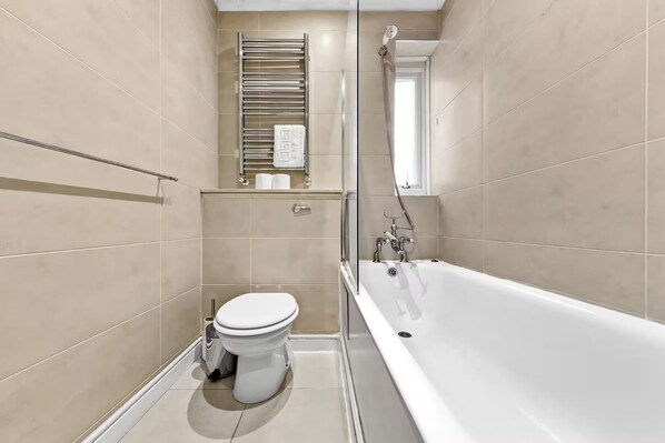A modern bathroom with a bathtub, toilet, and a towel rack. - Charming 2 Bedroom Retreat, Steps from Station! (London)