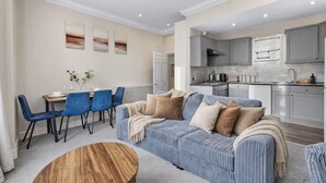 Ein modernes Wohnzimmer mit einer Couch, Sesseln, einem Esstisch und einer Küchenzeile.