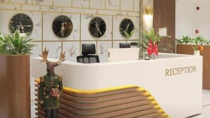 Un mostrador de recepción con un cartel que dice 'RECEPTION', rodeado de relojes en la pared, plantas en macetas y una figura decorativa.