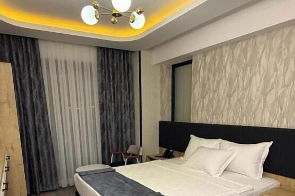 A modern hotel room with a large bed, a desk, and a wardrobe.