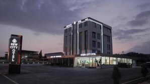 A modern hotel with a prominent sign, a parking lot, and a clear sky. - New City Otel (Osmaniye)