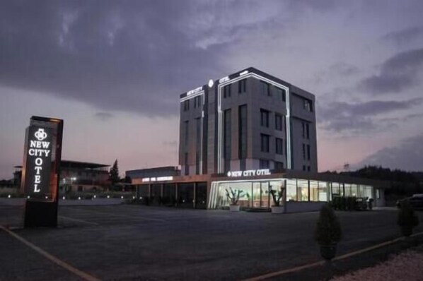 A modern hotel with a prominent sign, a parking lot, and a clear sky.