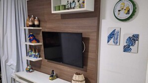 Olohuone, jossa on litteänäyttöinen televisio, puuhyllyt, valkoinen konsolipöytä ja roskakori.