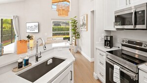 Una cocina moderna con armarios blancos, electrodomésticos de acero inoxidable, una isla grande con pileta y vistas a zonas verdes.