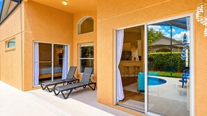 Una casa con un porche cubierto, piscina y puerta corrediza de vidrio que da a una cocina.