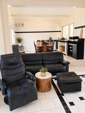 Ein modernes Wohnzimmer mit einer schwarzen Ledersofa, einem Holztisch und einer Essecke mit einem schwarz-weißen Fliesenspiegel.