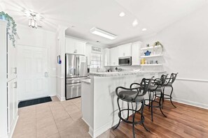 A modern kitchen with white cabinetry, stainless steel appliances, and a bar area with stools. - Magnolia Pointe Luster Leaf 4847-402 | Myrtlewood Condo | Golf, Pool & Fitness (Myrtle Beach)