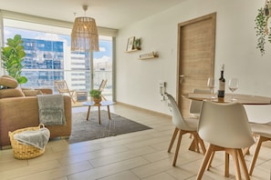 A modern living room with a sofa, dining table, chairs, a hanging light fixture, and a view of a cityscape through large windows. - Lovely apartment + balcony in La Carolina (Quito)