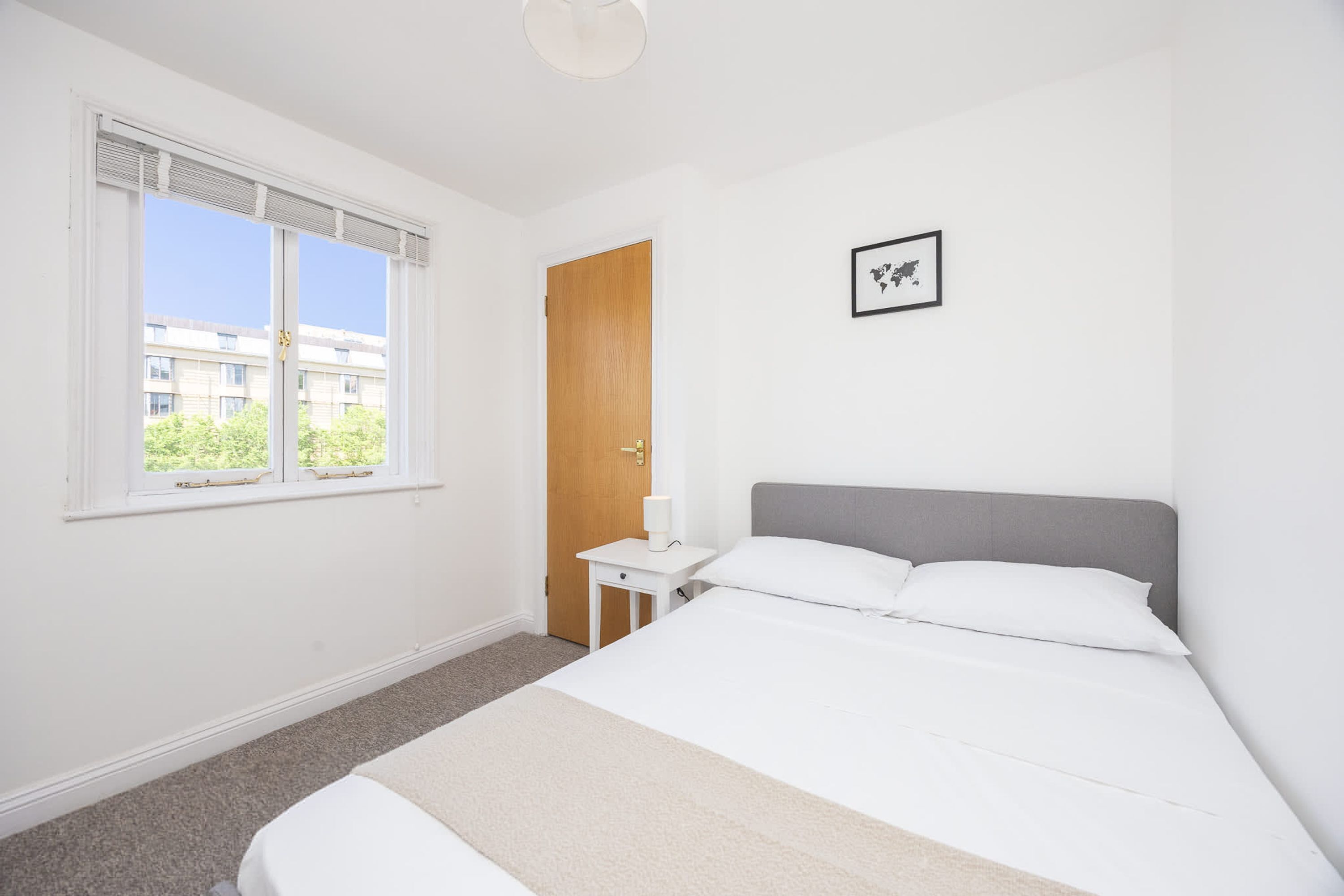 Un dormitorio con cama, mesita de noche, ventana y puerta.