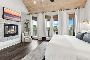Ein Schlafzimmer mit Kamin, einem großen Bett, Blick ins Freie und Deckenventilator.
