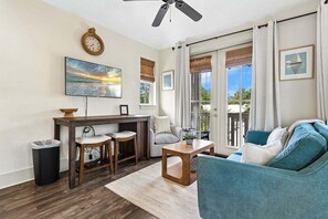 Ein Wohnzimmer mit Holztisch, Barhocker, einer Couch, einem Deckenventilator, einem Fernseher und einem Fenster mit Vorhängen.