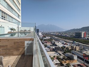 Un bâtiment moderne doté d’une piscine sur le toit, de rampes en verre et offrant une vue sur le paysage urbain et les montagnes.