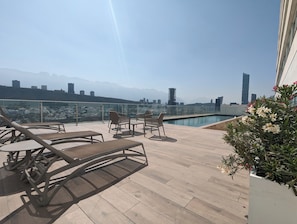 Terraza en la azotea con sillones de descanso, piscina y vistas a la ciudad.