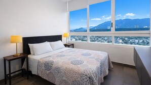 Ein Hotelzimmer mit einem Bett, zwei Nachttischlampen und einem Fenster mit Blick auf Stadt und Berge.