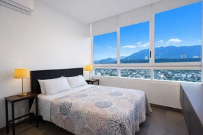 A hotel room with a bed, two bedside lamps, a window with a city and mountain view. - Iconic Cerro Views Retreat with Rooftop Pool (Monterrey)