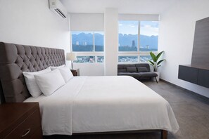 Une chambre d’hôtel moderne avec un grand lit, un canapé, une plante en pot et une vue sur la ville.