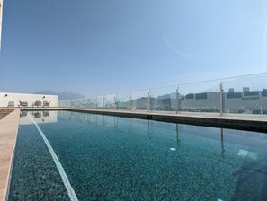 A clear swimming pool with a tiled edge, a glass railing, and a view of a cityscape with mountains in the distance. - Iconic Cerro Views Retreat with Rooftop Pool (Monterrey)