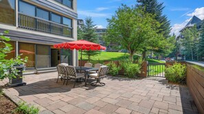 Eine Terrassensitzgelegenheit im Freien mit Tisch, Stühlen und rotem Sonnenschirm, mit Blick auf ein Gebäude und Bäume.