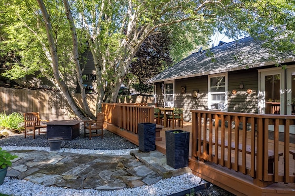 A wooden deck with outdoor furniture, a stone patio, and a house with a covered porch.