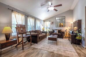 A living room with a ceiling fan, two sofas, a coffee table, a lamp, a guitar, and a mirror.