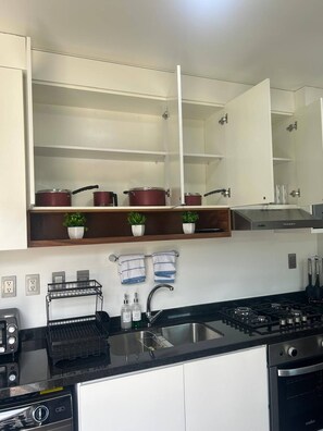 Una cocina moderna con armarios blancos, encimera negra, estufa, fregadero y un espejo sobre los estantes.