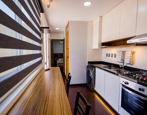 A compact kitchen with a wooden dining table, a built-in oven, and a dishwasher. - Container Glamping (Zapopan)