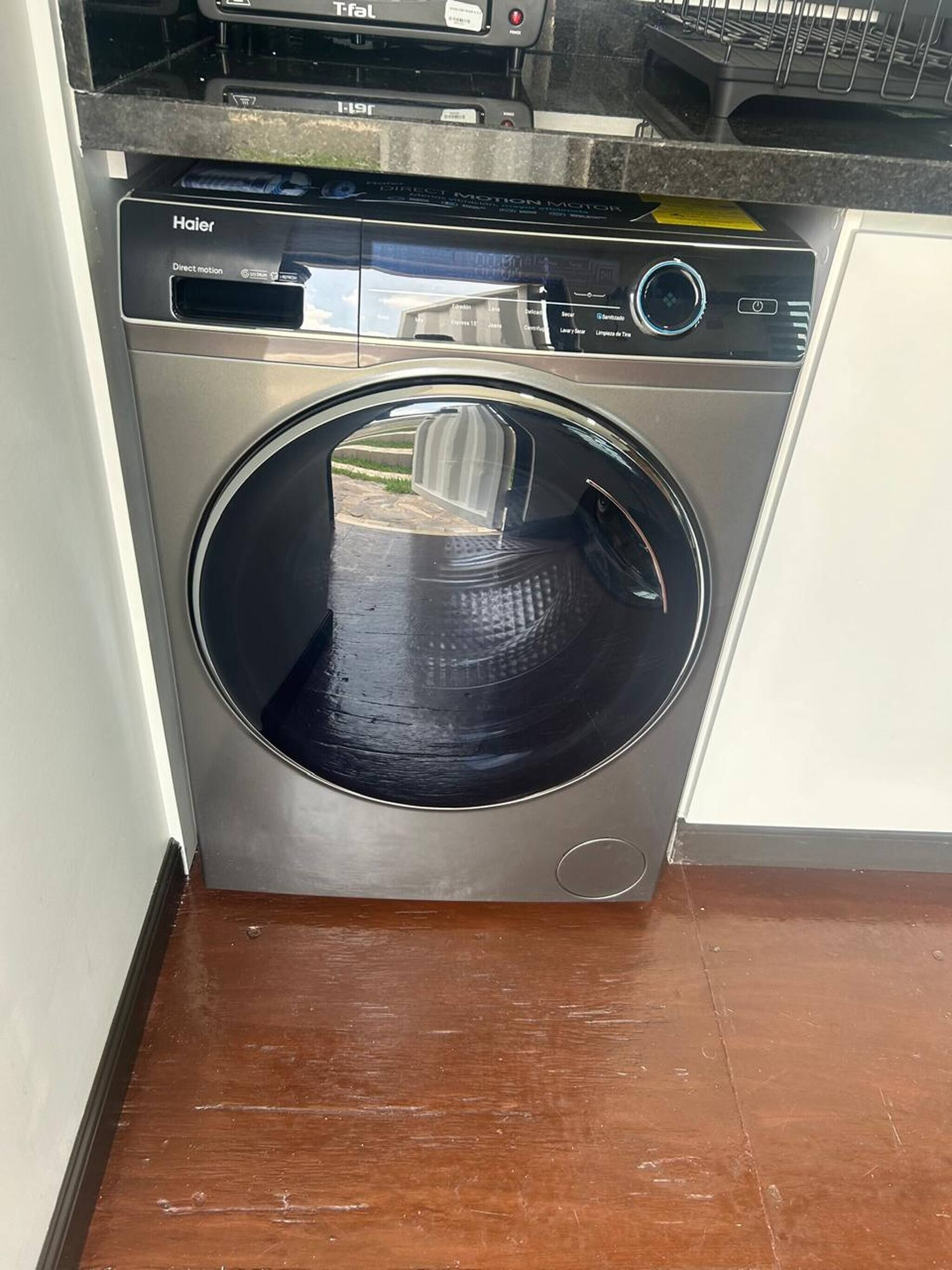 Un appareil compact, en acier inoxydable, combinant une machine à laver et un sèche-linge à chargement frontal, doté d’un panneau de commande et d’un écran numérique.