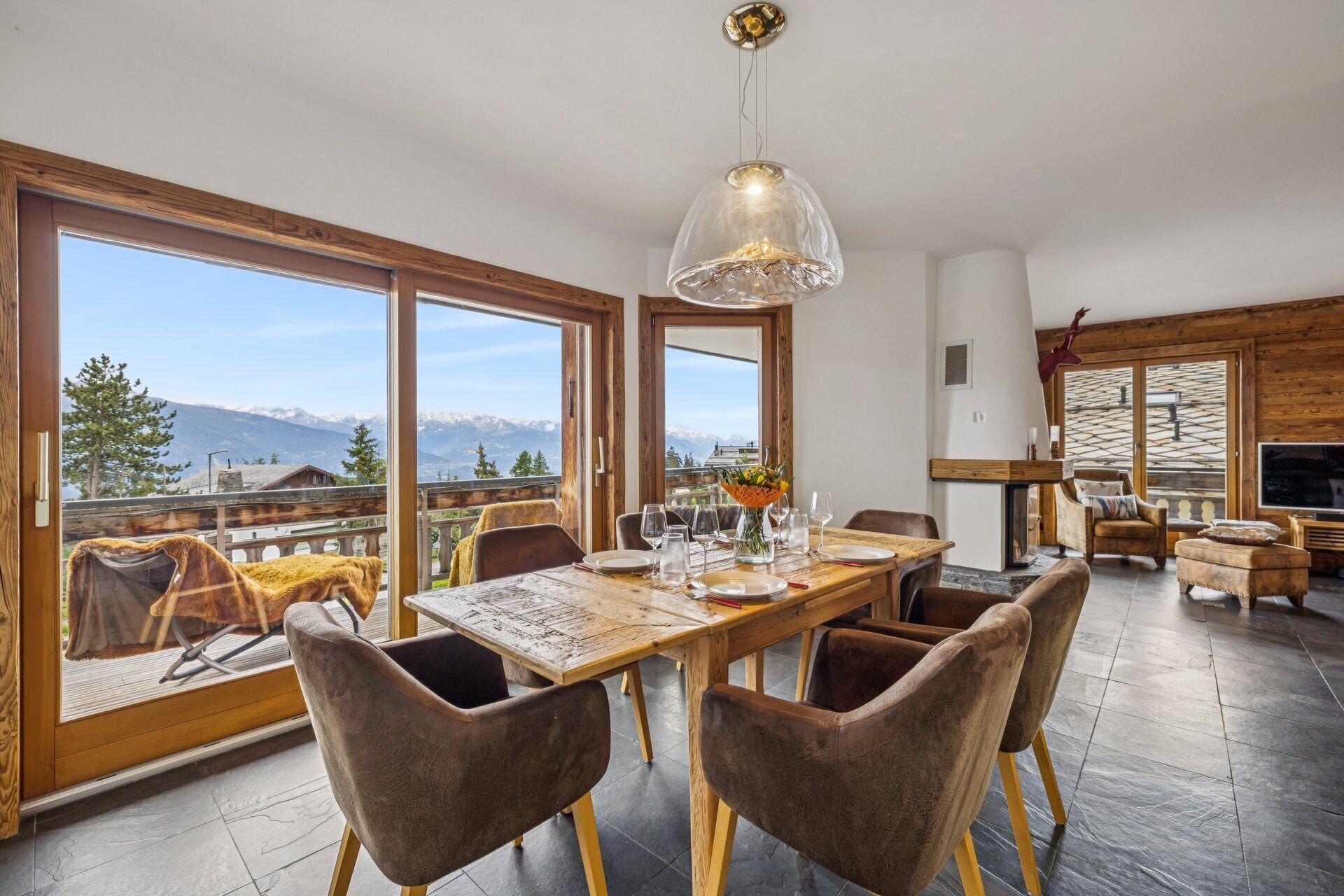 A dining area with a table set for four, large windows, and a view of mountains.