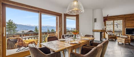 A dining area with a table set for four, large windows, and a view of mountains.