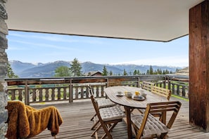 Eine Holterrasse mit rundem Tisch und Stühlen, mit Blick auf eine gebirgige Landschaft.