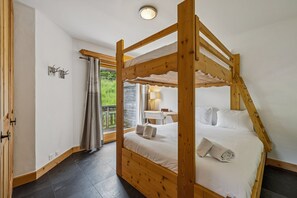 Un lit à baldaquin en bois, avec une literie blanche, un petit bureau avec une lampe et une vue sur la verdure par la fenêtre.