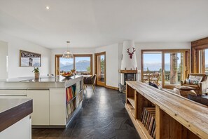 A modern kitchen with a central island, a fireplace, and a view of mountains through large windows. - Welcome to Chalet Infinity by Mrs Miggins, a stunning 140 sqm luxury alpine apartment ideally locate (Crans-Montana)