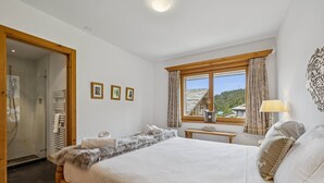 Un dormitori amb un llit gran, una finestra amb cortines, una tauleta de nit i una làmpada penjada a la paret.