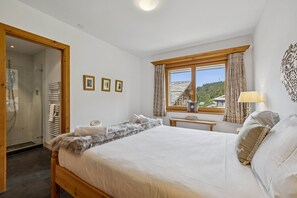 A bedroom with a large bed, a window with curtains, a bedside table, and a wall-mounted lamp. - Welcome to Chalet Infinity by Mrs Miggins, a stunning 140 sqm luxury alpine apartment ideally locate (Crans-Montana)