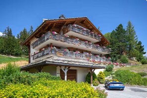 A multi-story chalet with balconies, surrounded by greenery and a parked car. - Welcome to Chalet Infinity by Mrs Miggins, a stunning 140 sqm luxury alpine apartment ideally locate (Crans-Montana)