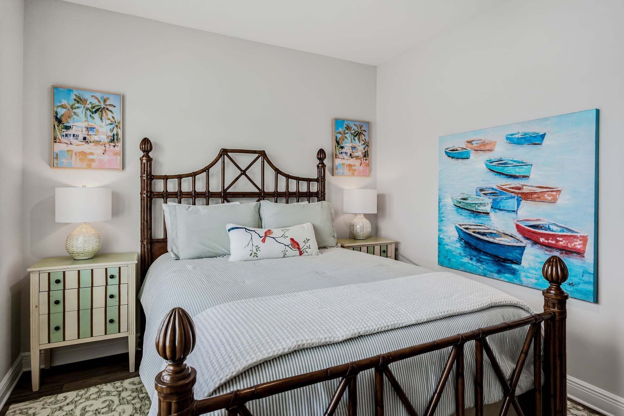A neatly made bed with a wooden headboard, two bedside tables with lamps, and a large painting of boats on the wall.