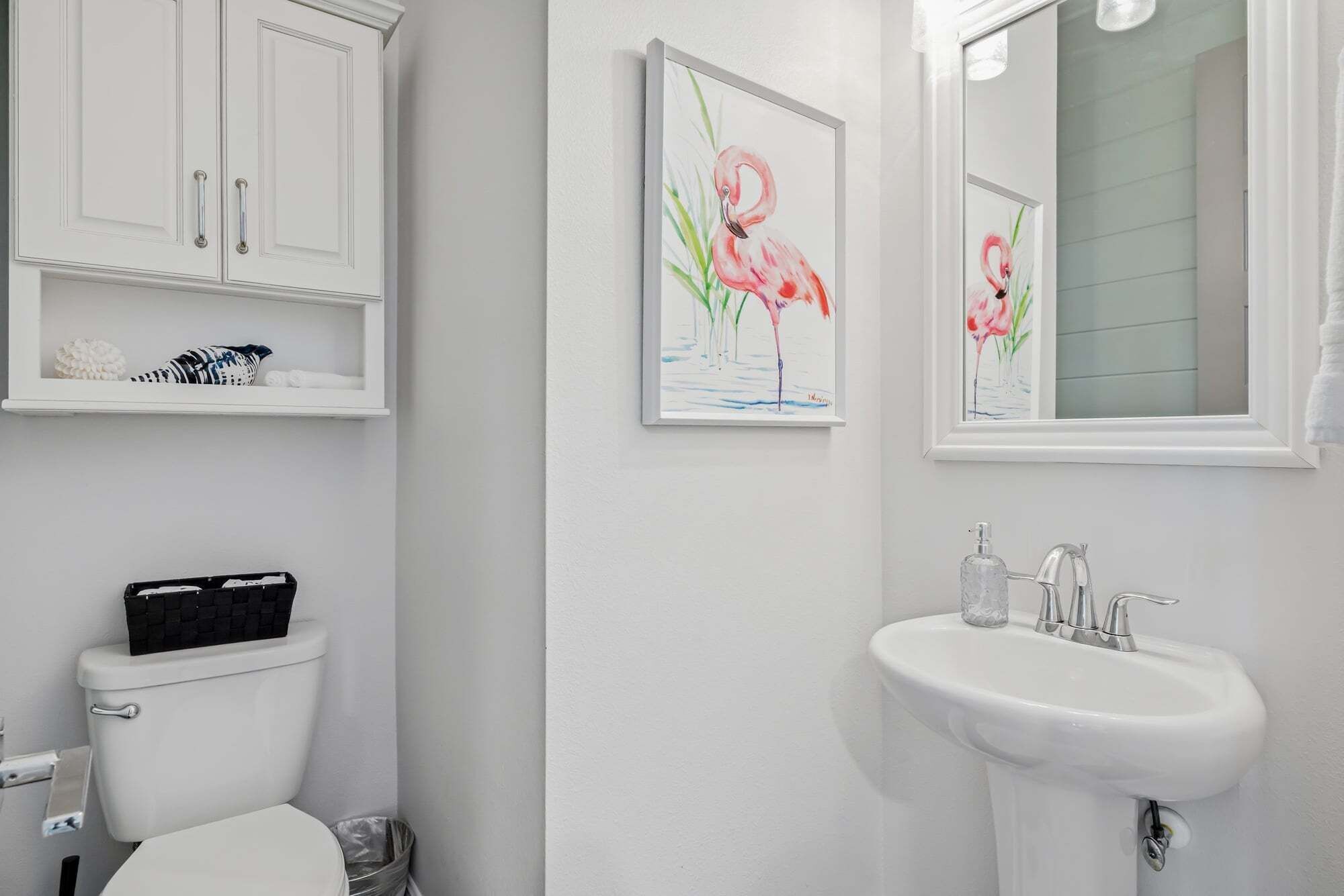 A bathroom with a toilet, a sink, and two framed paintings of flamingos.