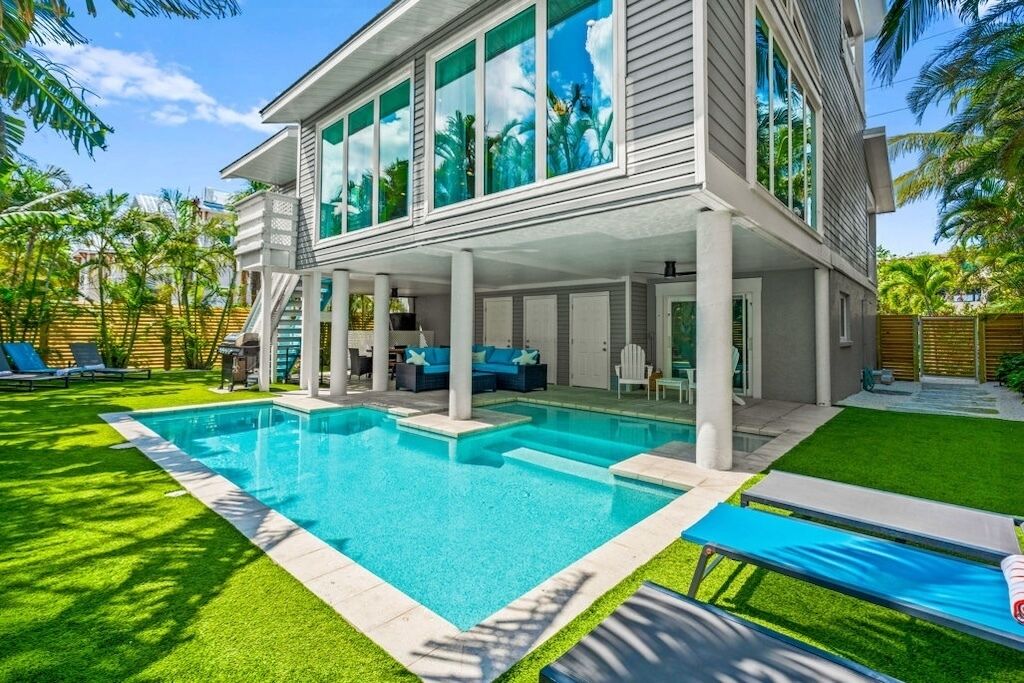 Una casa moderna con piscina, patio cubierto y césped cuidado.
