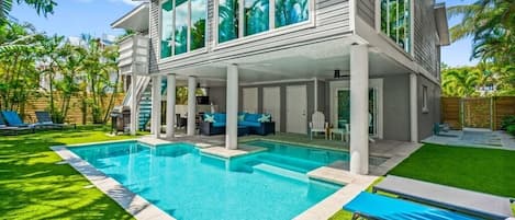 Una casa moderna con piscina, patio cubierto y césped cuidado.