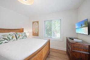 A bedroom with a bed, a window with blinds, a dresser, and a TV on the wall. - The Palm at Bean Point - Luxury Coastal Retreat with Heated Pool, Walk to Beach (Anna Maria)