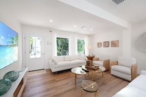 A modern living room with a white sofa, two armchairs, a coffee table, and a TV on a wall. - The Palm at Bean Point - Luxury Coastal Retreat with Heated Pool, Walk to Beach (Anna Maria)