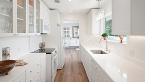 Una cucina moderna con mobili bianchi, pavimento in legno e vista sull'area pranzo.