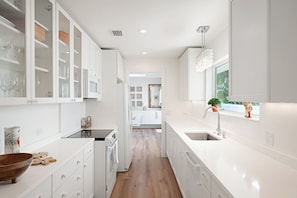 A modern kitchen with white cabinetry, a wooden floor, and a view into the dining area. - The Palm at Bean Point - Luxury Coastal Retreat with Heated Pool, Walk to Beach (Anna Maria)